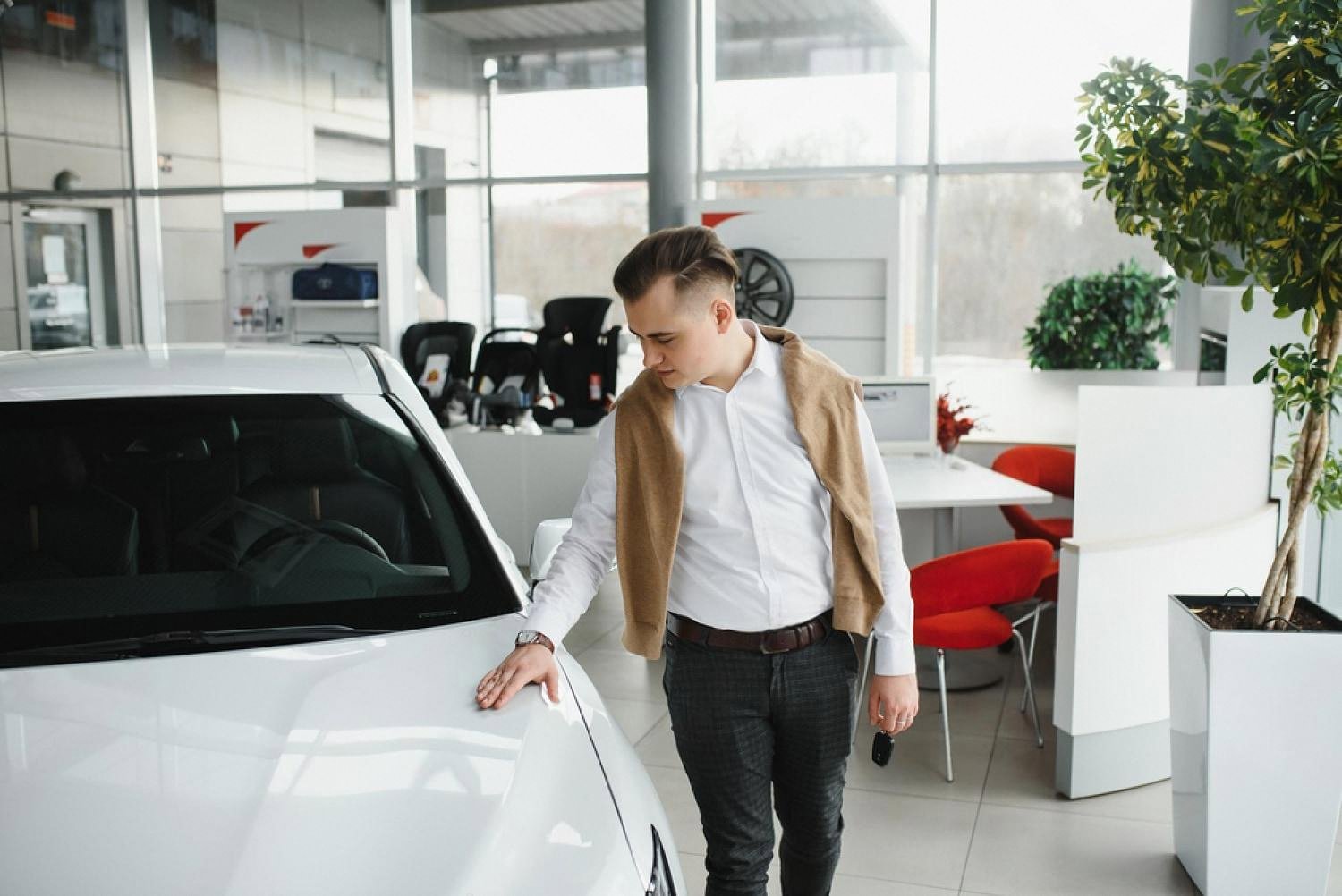 Young man inspecting a white rental car in a showroom before signing the contract