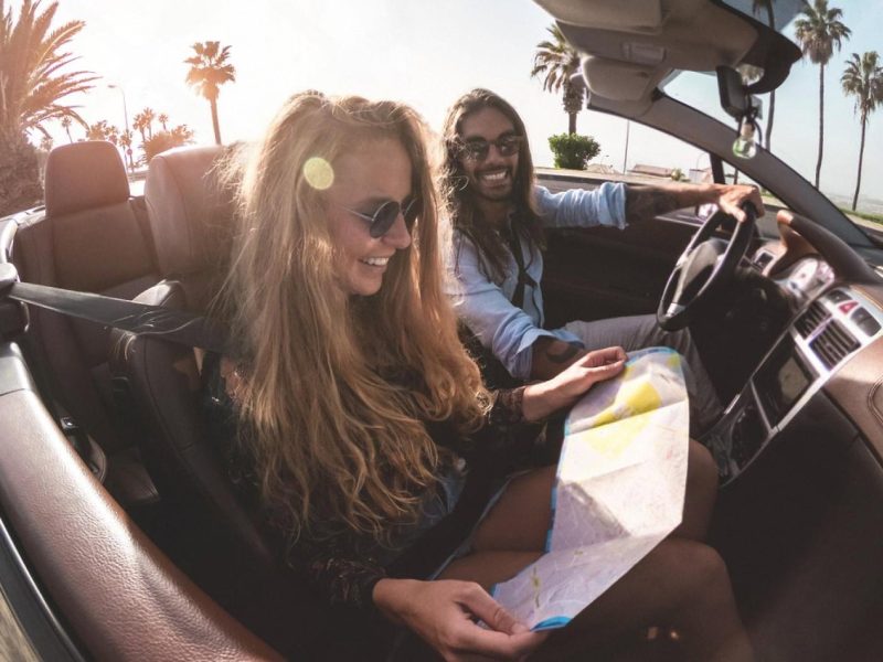 Couple driving a convertible on an Australian coastal road with a paper map