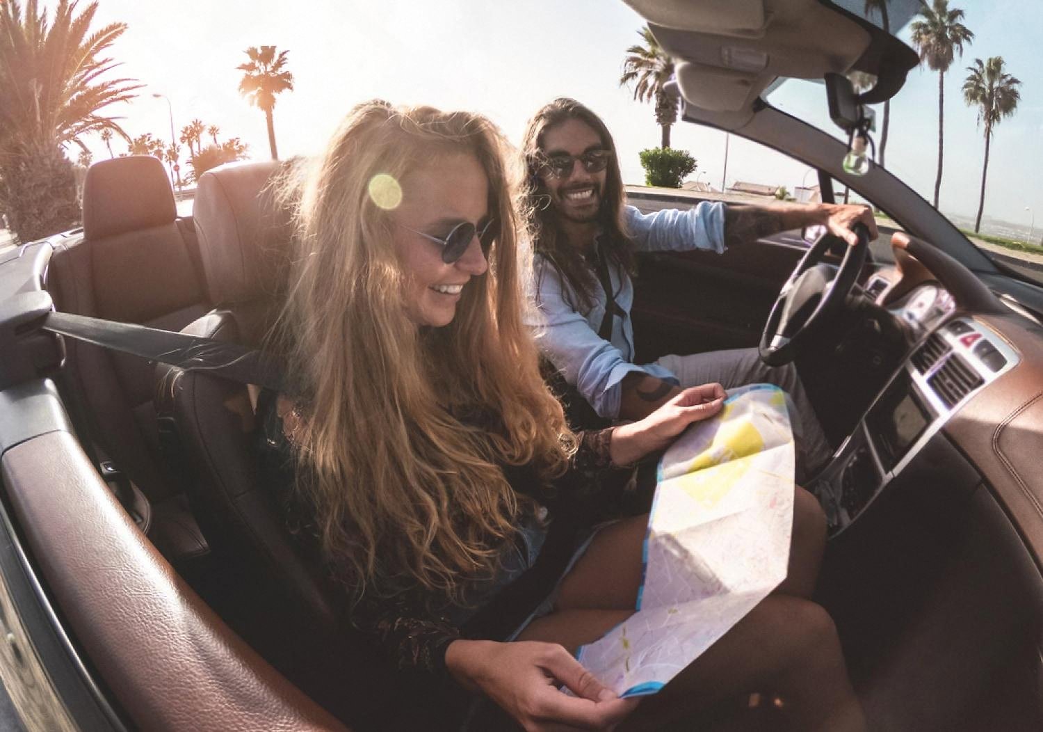 Couple driving a convertible on an Australian coastal road with a paper map